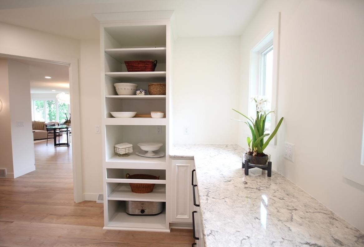 Light-filled pantry and prep space with open shelving and stone countertops in a custom home by Ross Construction in Marathon, WI