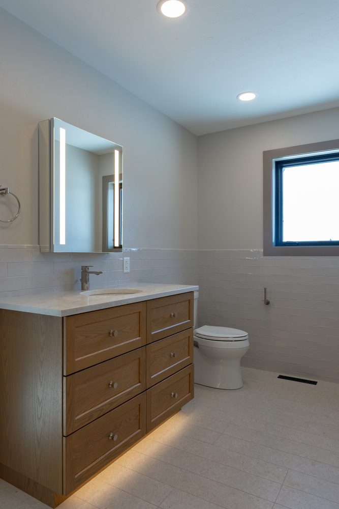 Modern bathroom with wood vanity and LED mirror in custom home by Ross Construction in Rib Mountain, WI.
