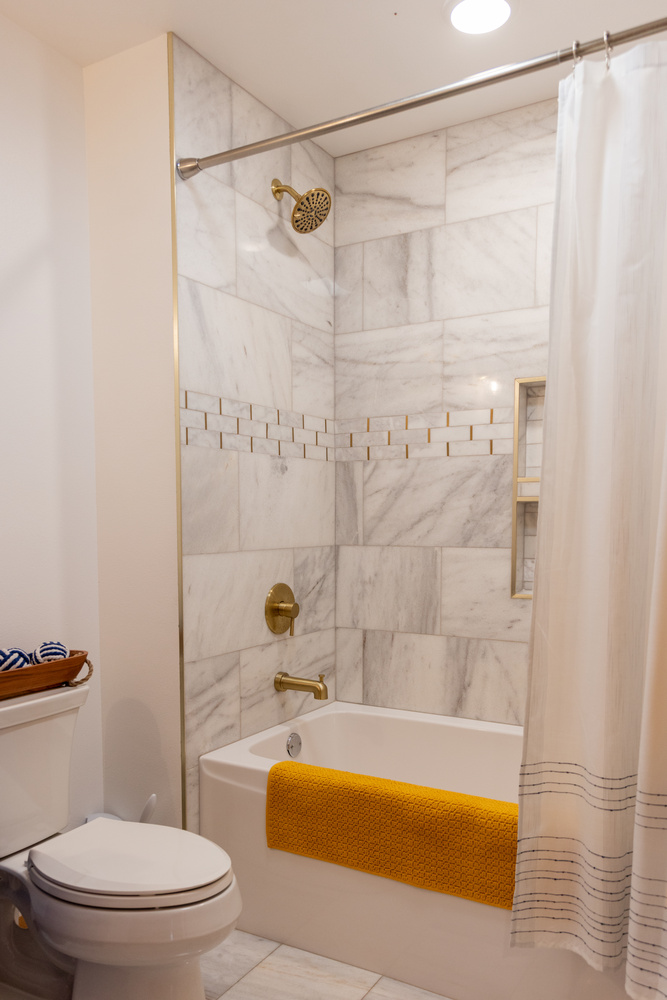 Elegant marble-tiled bathtub and shower with gold fixtures in Marathon, WI home by Ross Construction.