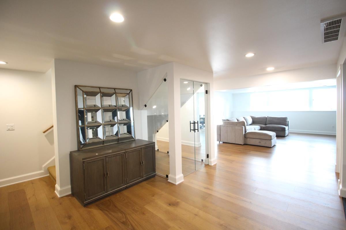 Bright lower level with glass-enclosed stairway and sectional sofa in a Ross Construction custom home in Lake Dubay, WI
