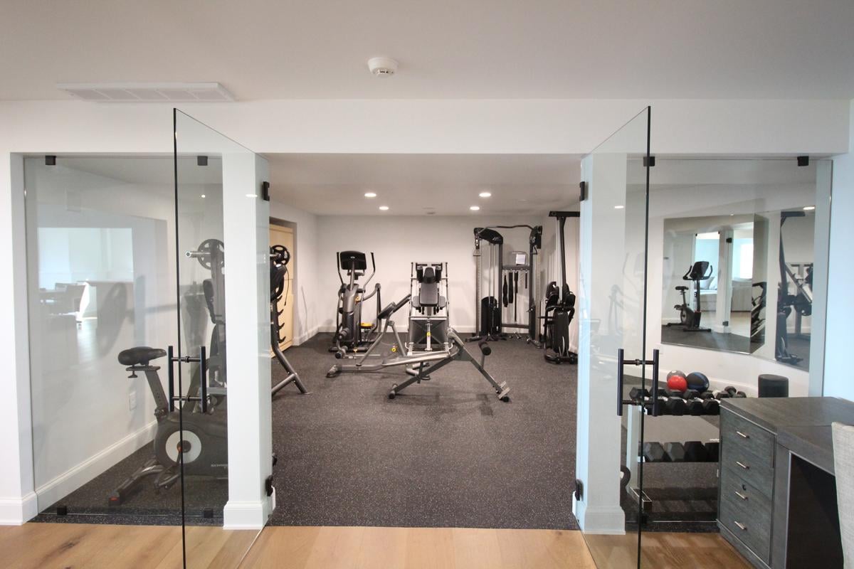 Glass double doors open to home gym with cardio and strength training equipment by Ross Construction in Lake Dubay, WI