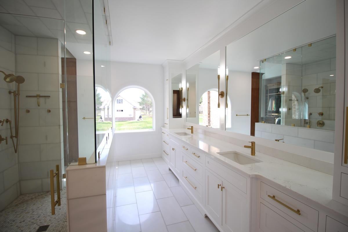 Luxurious double vanity bathroom with gold fixtures and natural light by Ross Construction in Marathon, WI