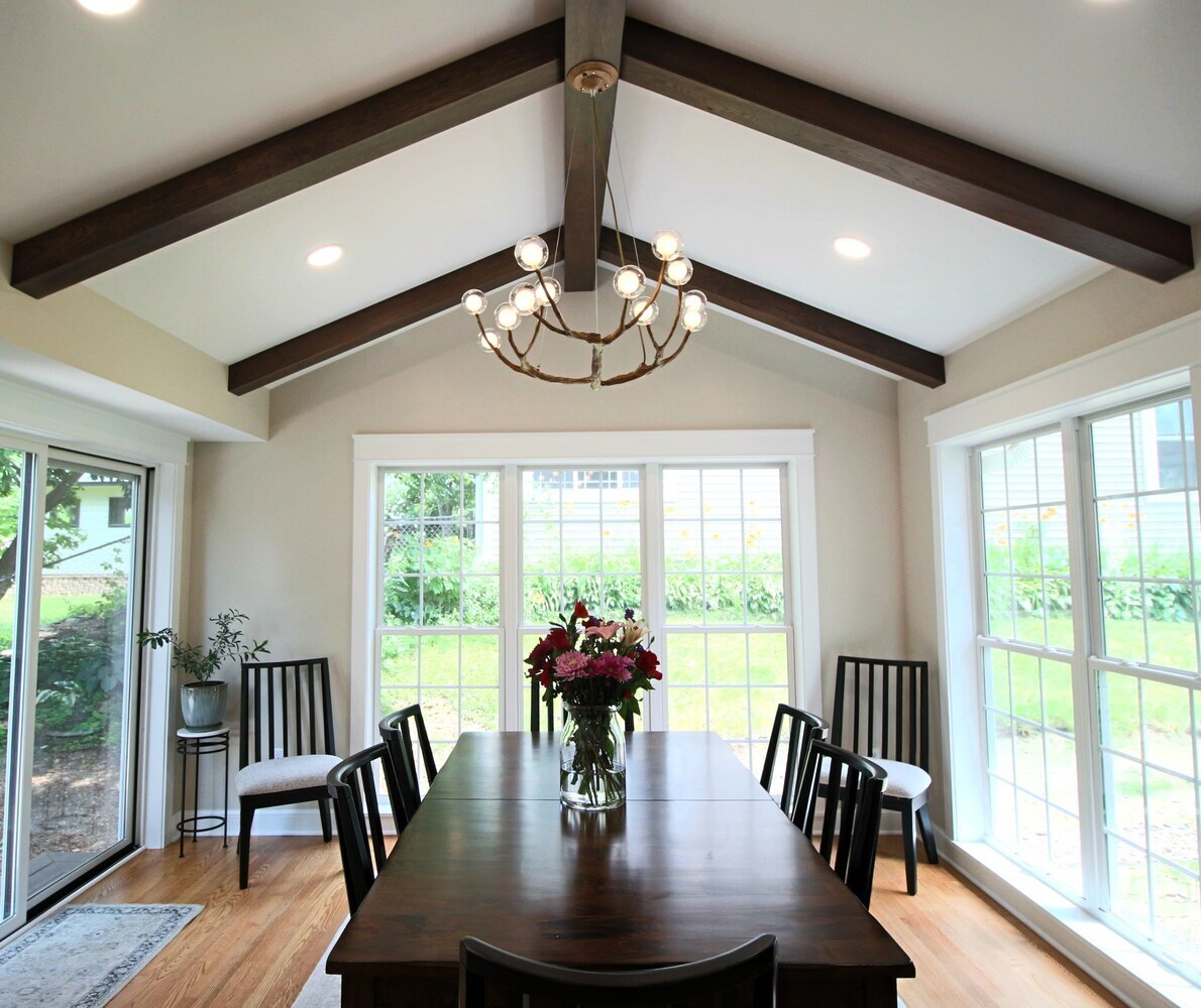 Dining room with exposed wood beams and panoramic windows by Ross Construction in Marathon, WI.
