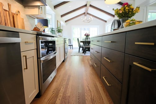 Galley kitchen view with dark island cabinetry and open dining space by Ross Construction in Lake Dubay, WI.