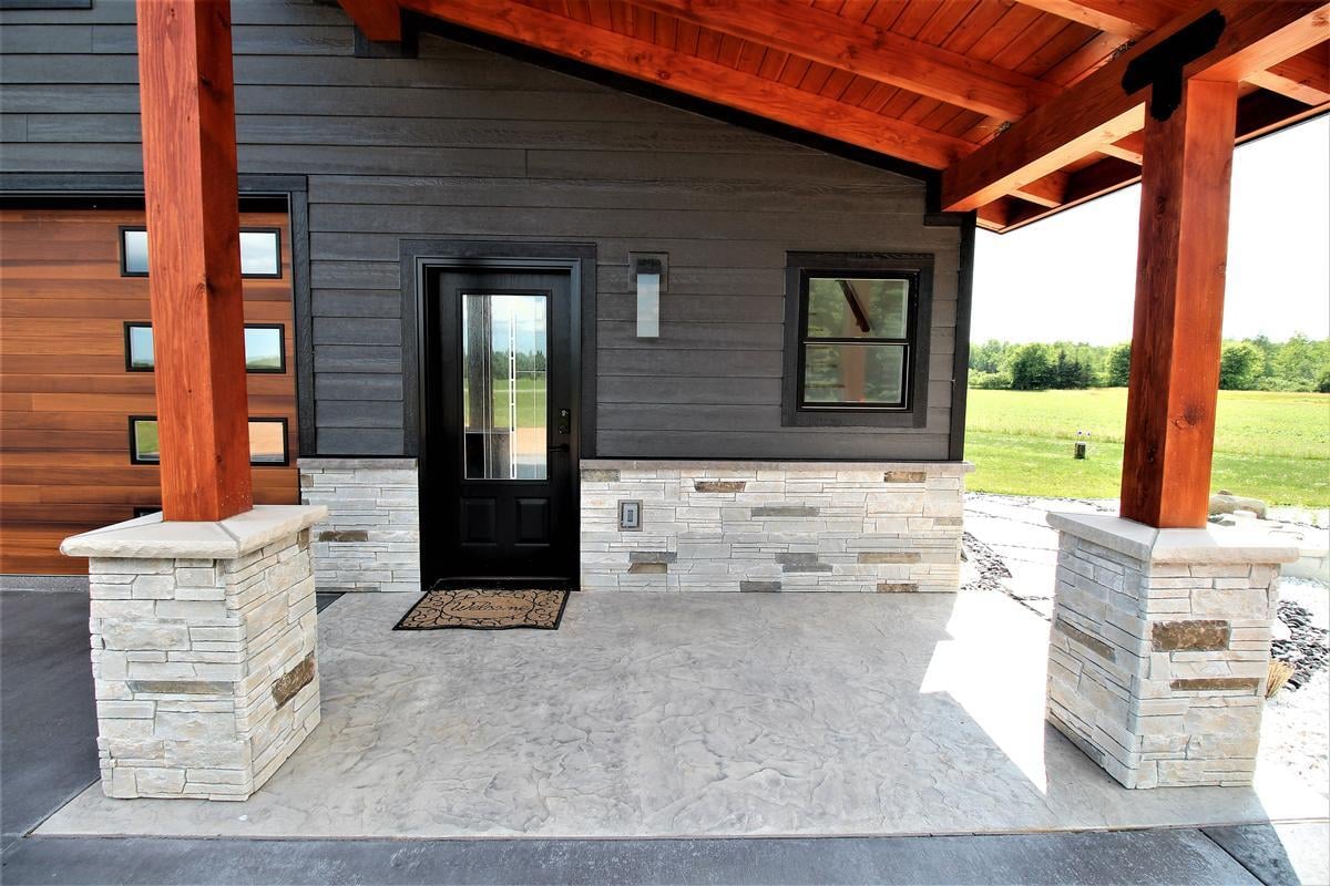 Front entryway of a modern custom home in Marathon, WI by Ross Construction with stone pillars and black siding.