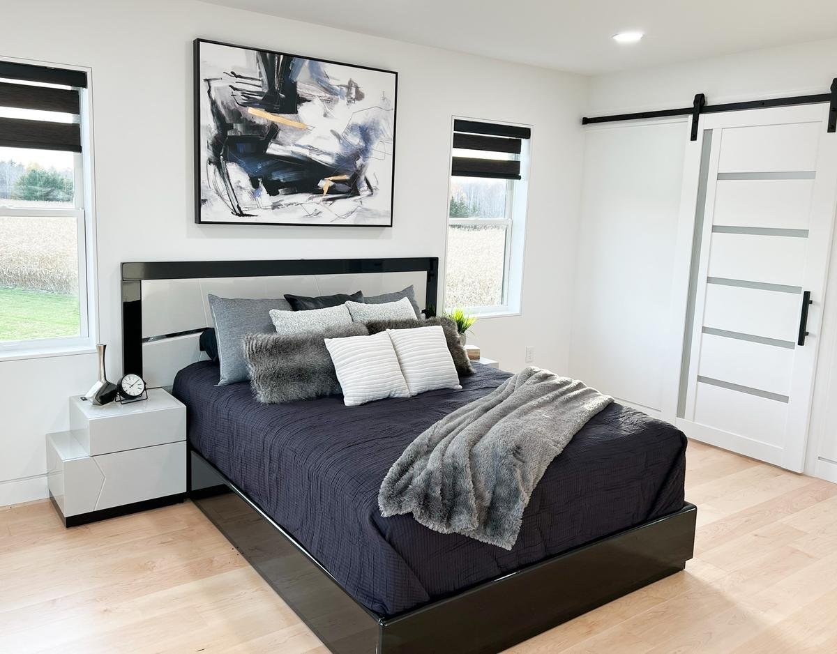 Modern master bedroom in custom Marathon, WI home by Ross Construction featuring black bed frame and abstract wall art.