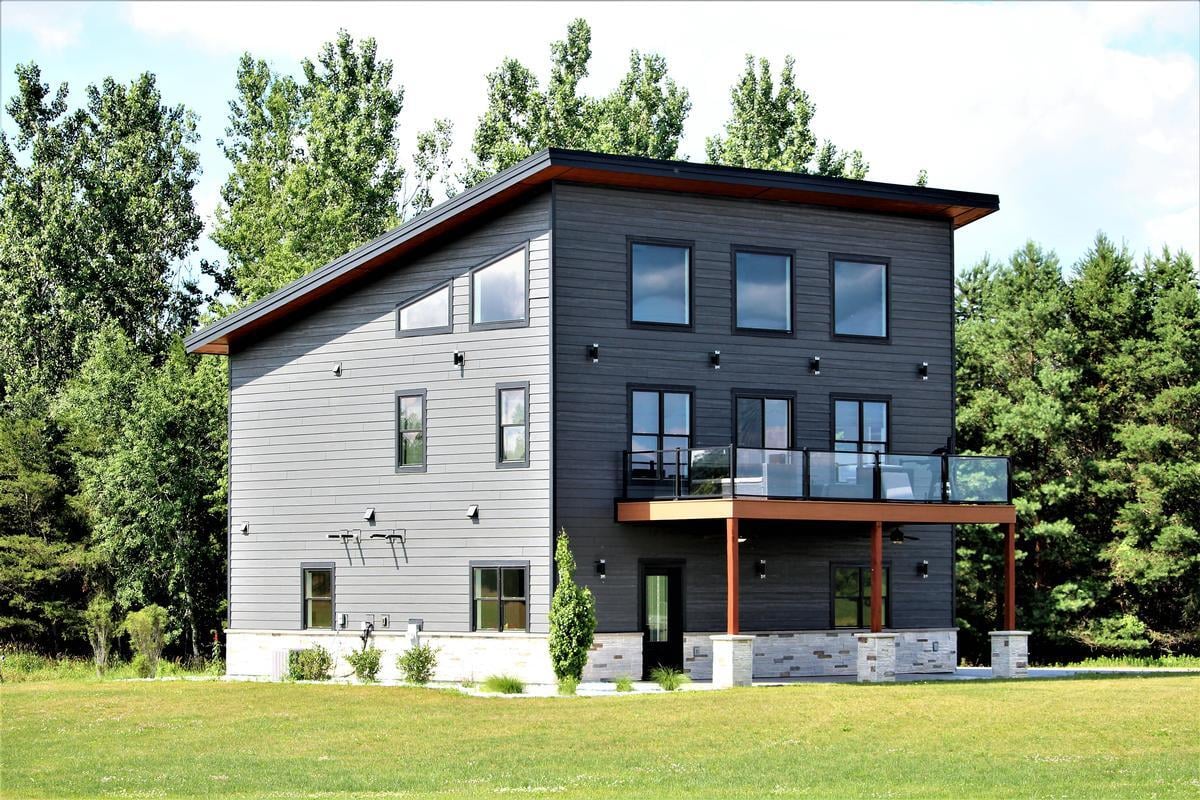Rear exterior of modern custom home by Ross Construction in Rib Mountain, WI featuring large windows and balcony.