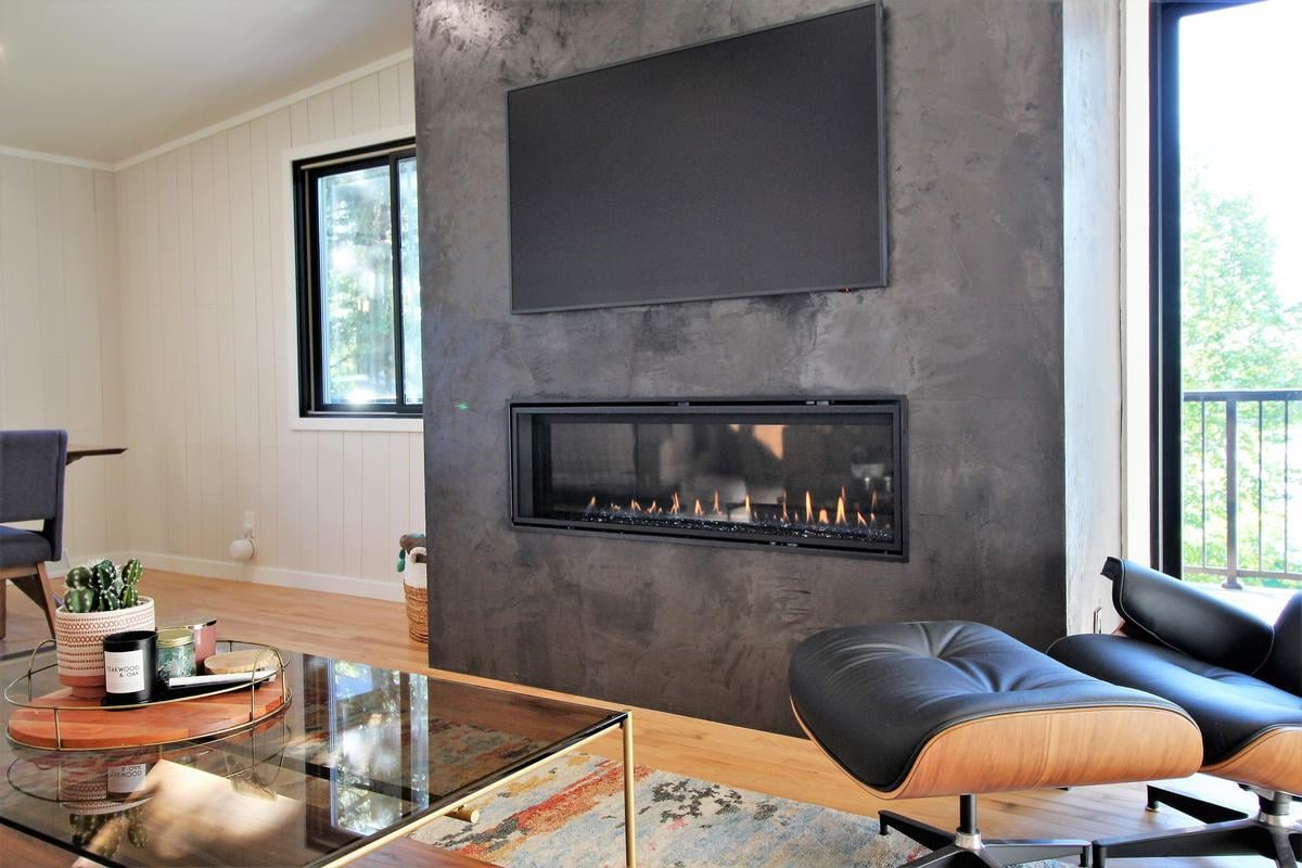 Modern fireplace feature wall with TV and Eames lounge chair in Lake Dubay custom home by Ross Construction.