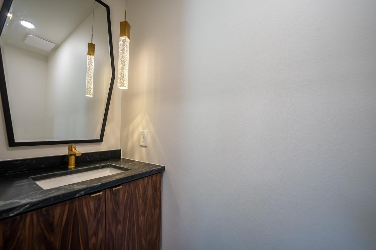 Powder room remodel in Wausau custom home by Ross Construction with geometric mirror and gold pendant lighting.