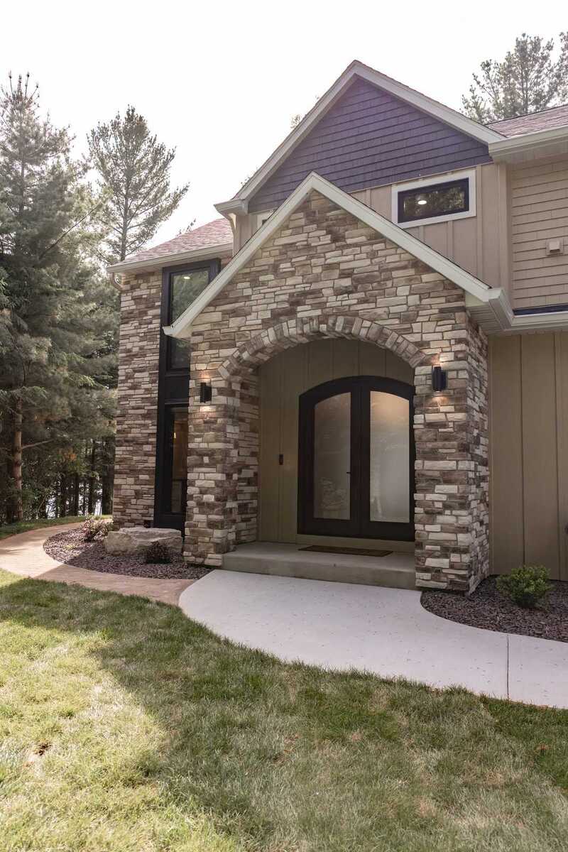 whole home remodel exterior stone gable entry with arched double doors and lawn minocqua wi