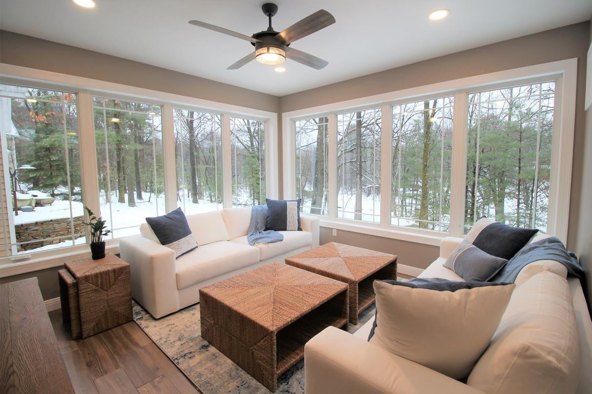 Forest-view sunroom with white seating and large windows by Ross Construction in Rib Mountain, WI.
