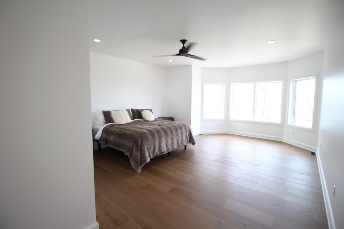 Minimalist primary bedroom with bay windows and hardwood floors by Ross Construction in Marathon, WI
