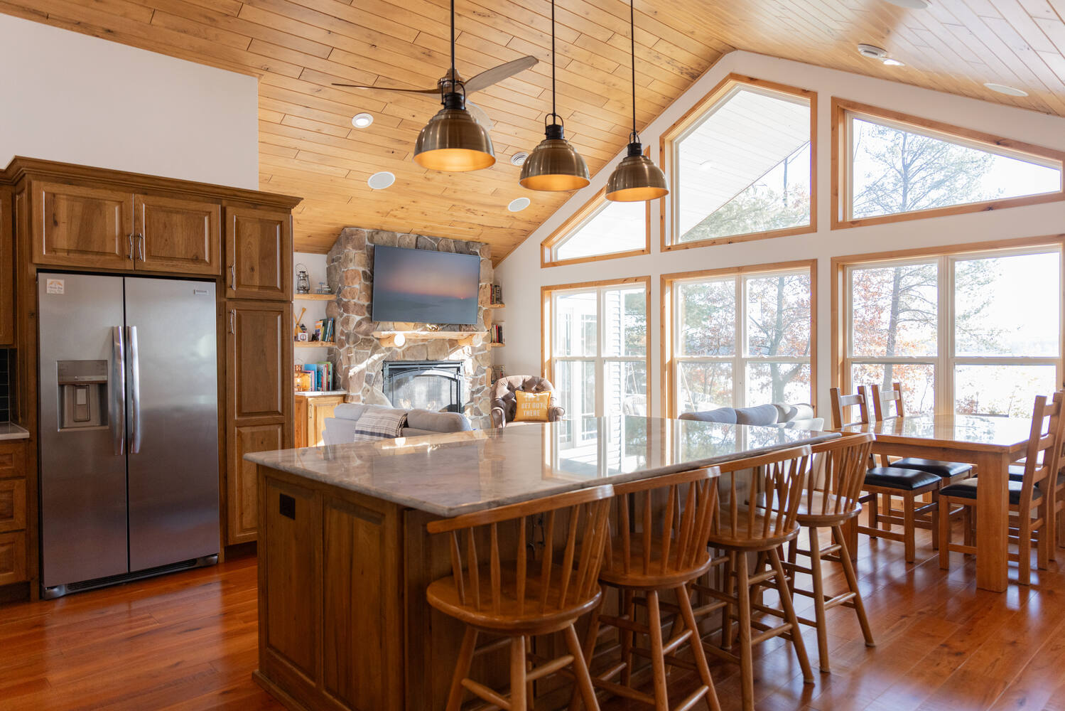 Open kitchen and dining area with stone fireplace and vaulted wood ceiling in Lake Dubay, WI home by Ross Construction.