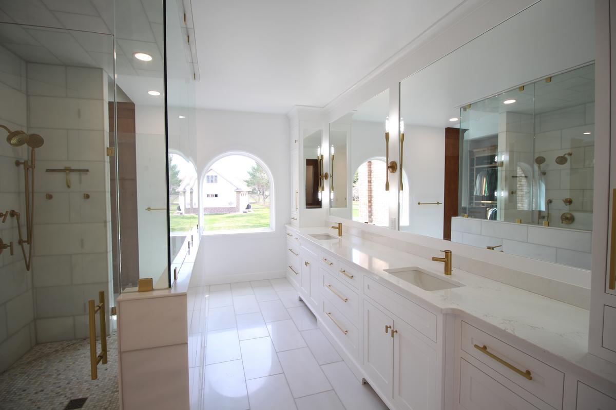 Luxurious double vanity bathroom with gold fixtures and natural light by Ross Construction in Marathon, WI