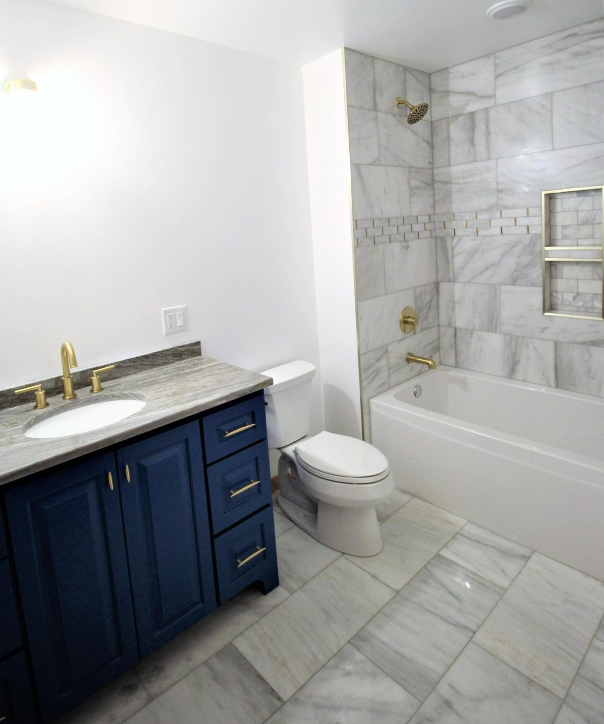 Sophisticated bathroom upgrade with navy vanity and marble flooring by Ross Construction in Lake Dubay, WI.