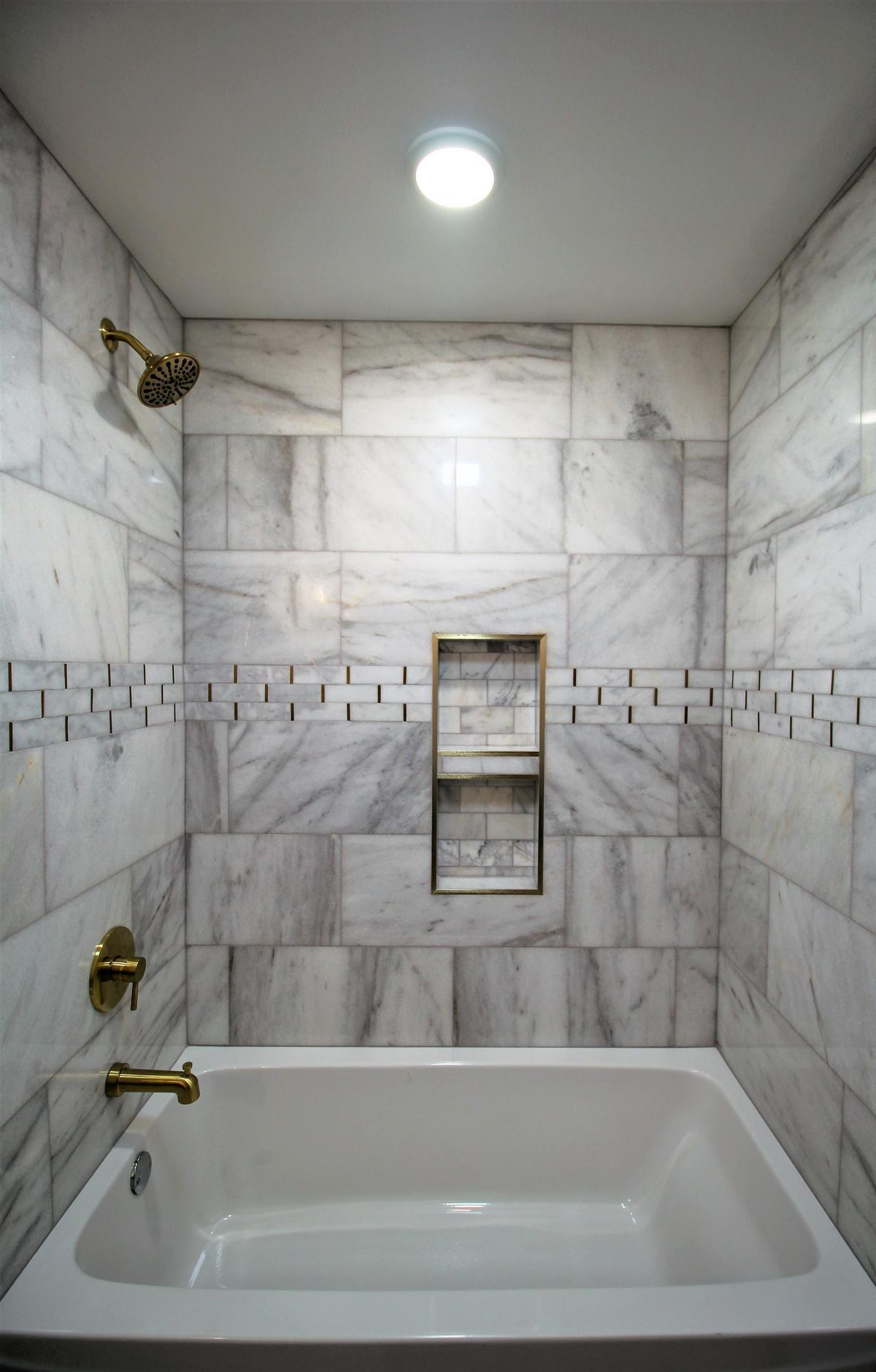 White tub and gold shower fixtures in custom marble bathroom remodel by Ross Construction in Rib Mountain, WI.
